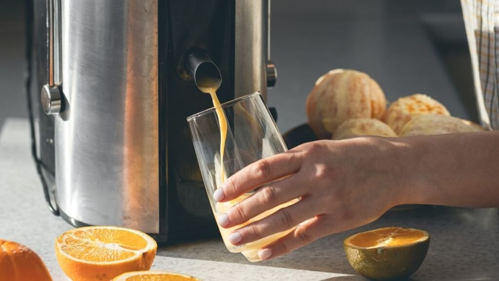 Mão de mulher coletando suco de laranja no espremedor elétrico.